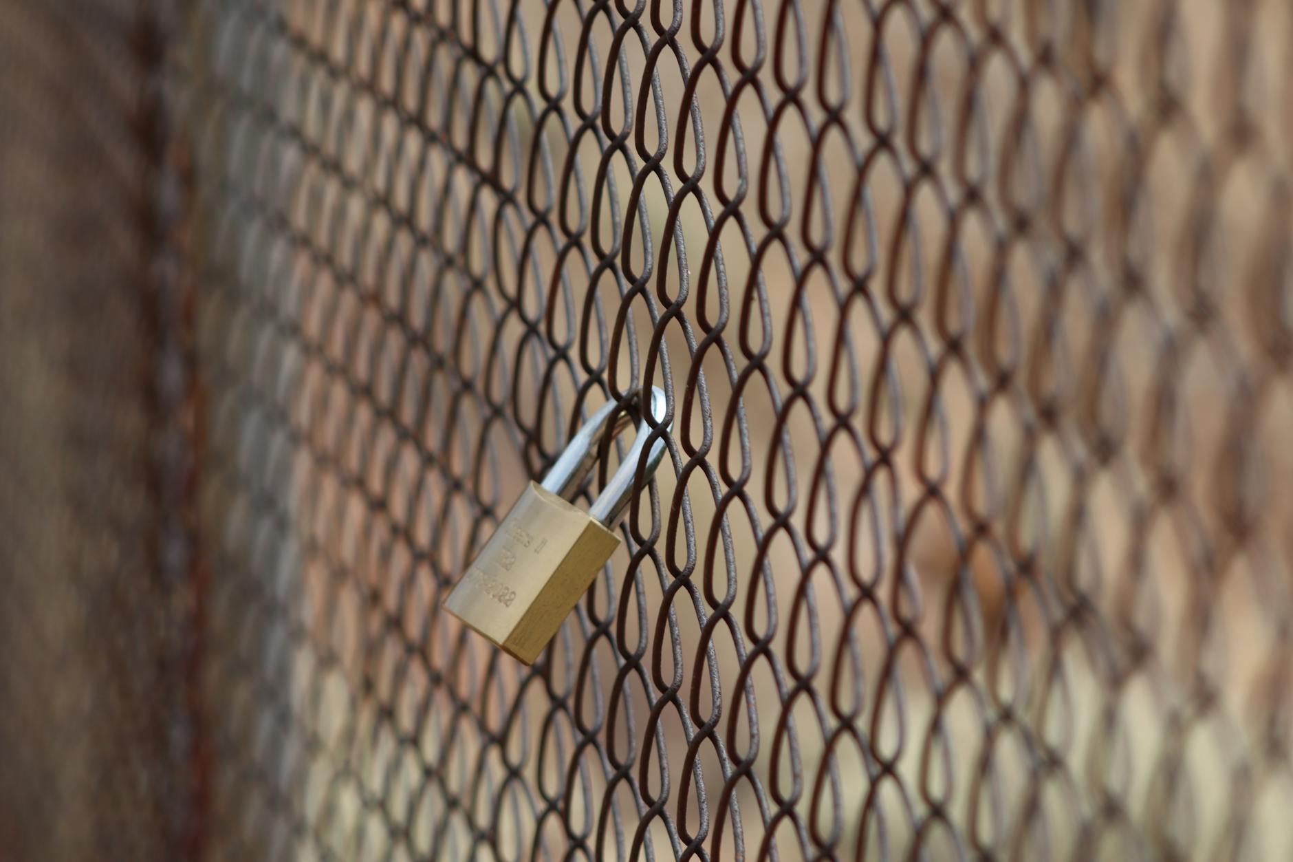 Kłódka na metalowym ogrodzeniu z siatki symbolizująca ochronę ogrodzenia