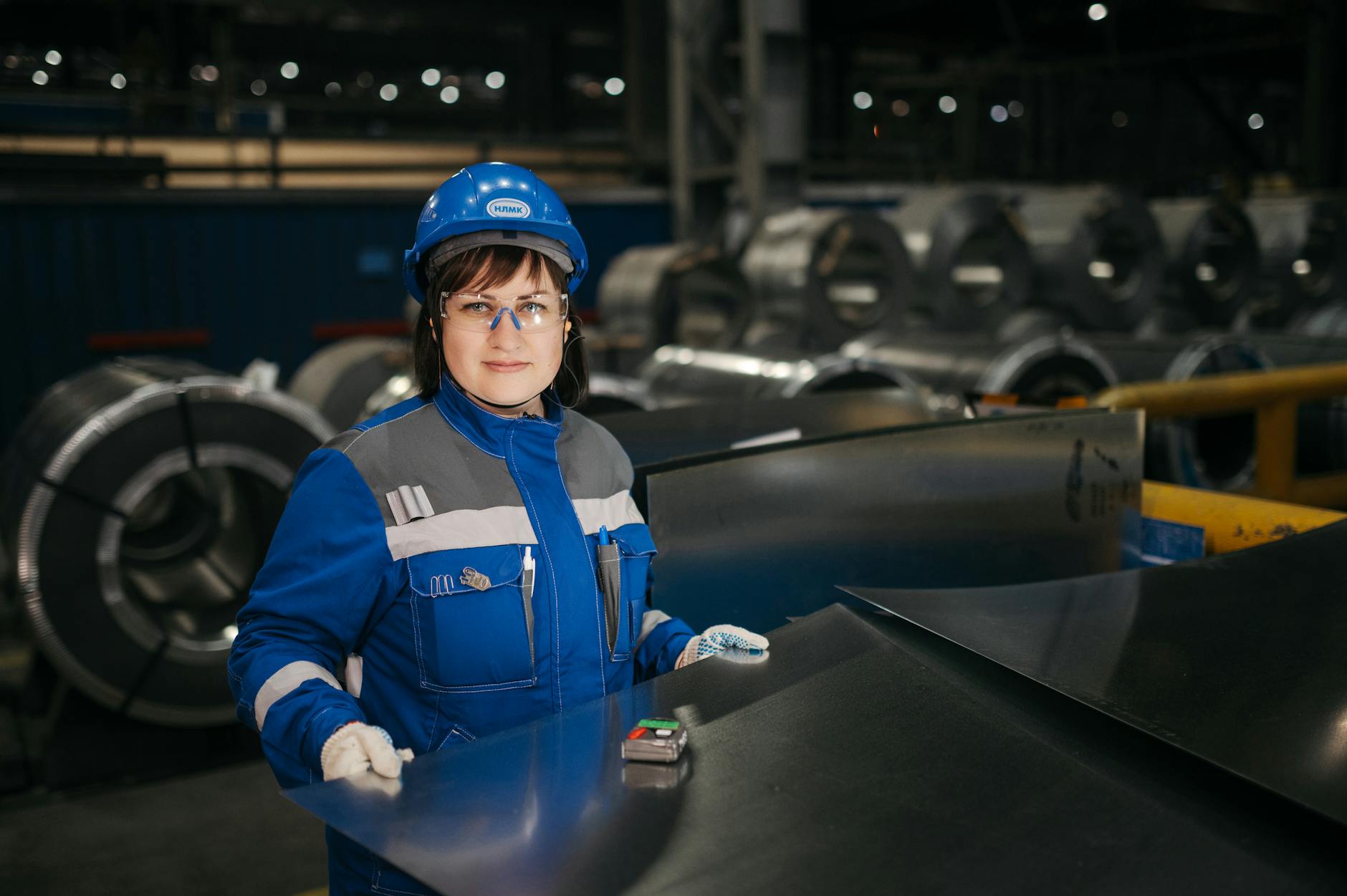 Pracowniczka w kasku kontroluje arkusze stali w nowoczesnej hali