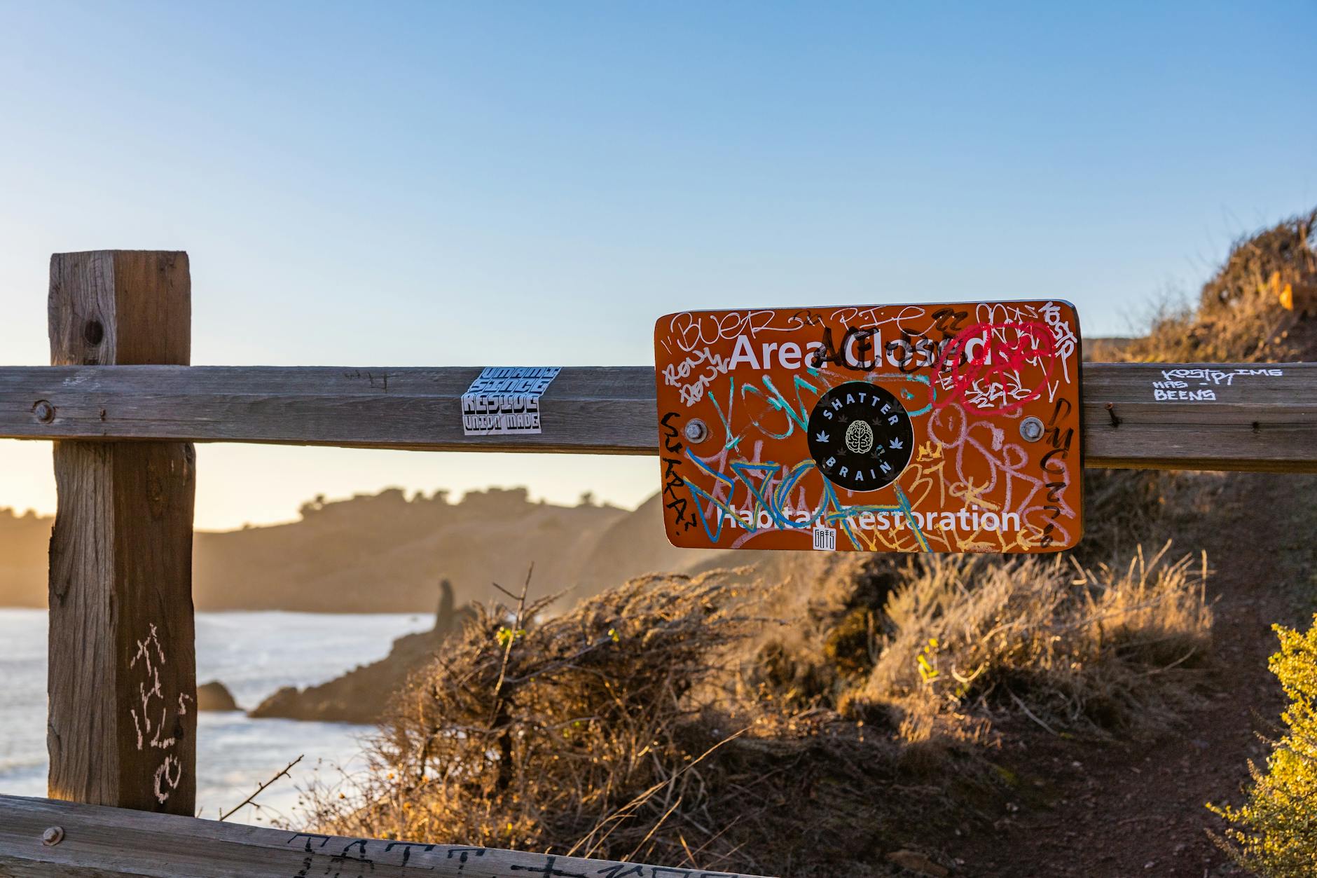 Zniszczony graffiti znak zakazu w zamkniętym drewnianym ogrodzeniu nad wodą