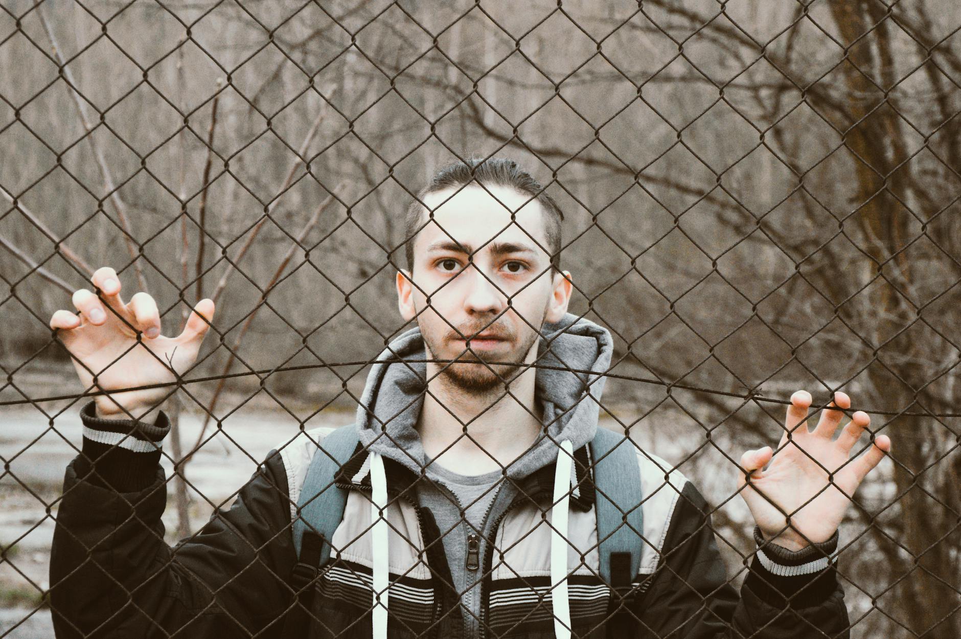 Młody mężczyzna za stalowym ogrodzeniem siatkowym zimą