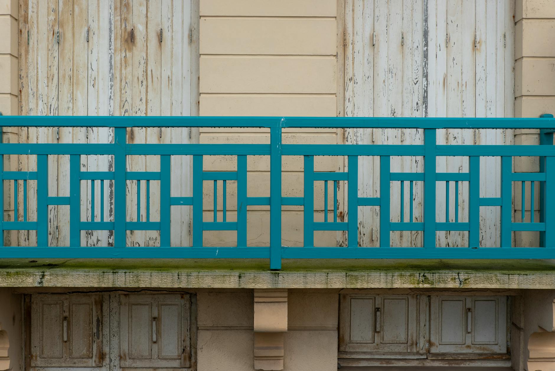 Stara balustrada balkonowa z niebieską poręczą i drewnianymi drzwiami